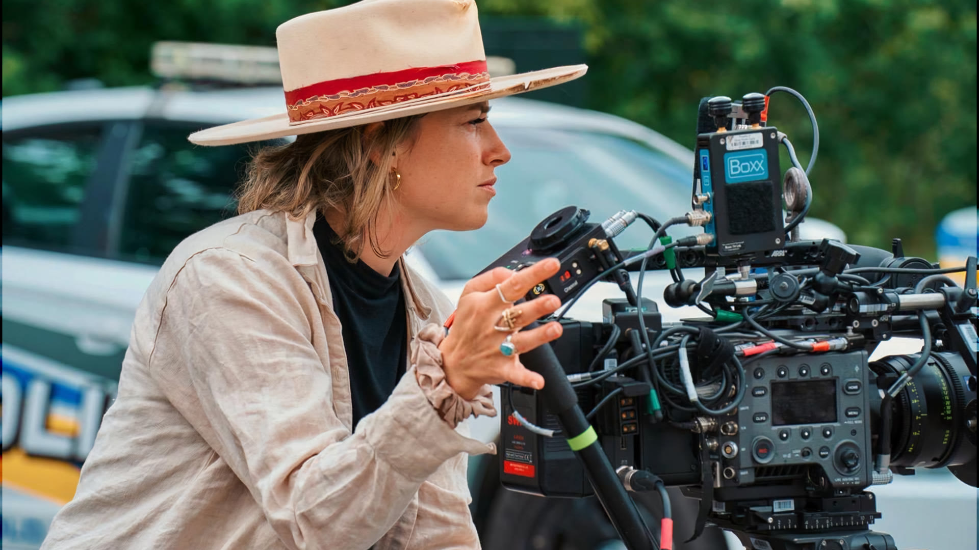 Angelia Hughes, in a wide-brimmed hat, operating a cinema camera on an exterior location.